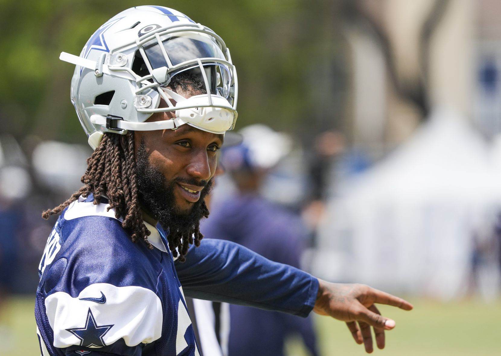 A football player in a Cowboys uniform and helmet points while standing outdoors during practice.