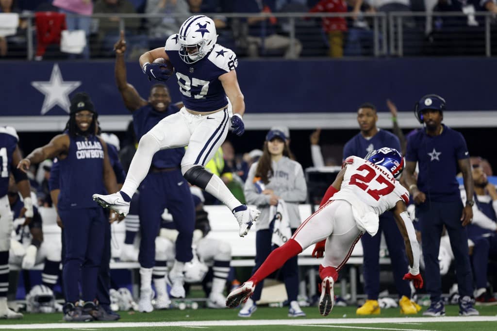 ARLINGTON, TEXAS - NOVEMBER 24: Jake Ferguson #87 of the Dallas Cowboys jumps over Jason Pinnock #27 of the New York Giants during the second half at AT&amp;T Stadium on November 24, 2022 in Arlington, Texas. Wesley Hitt/Getty Images/AFP (Photo by Wesley Hitt / GETTY IMAGES NORTH AMERICA / Getty Images via AFP)