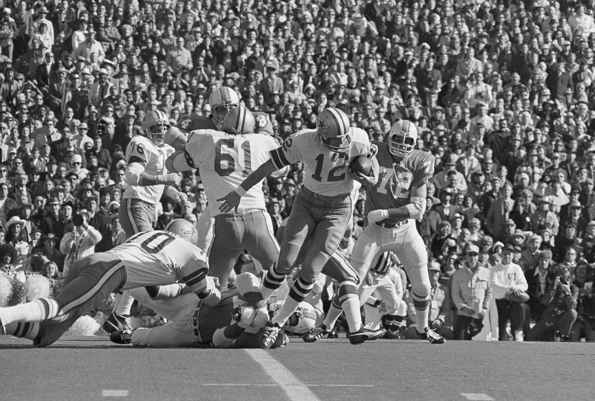 Black and white photo of a football game with players from both teams in action, featuring the Cowboys' legendary Roger Staubach. A crowd of spectators can be seen in the background.