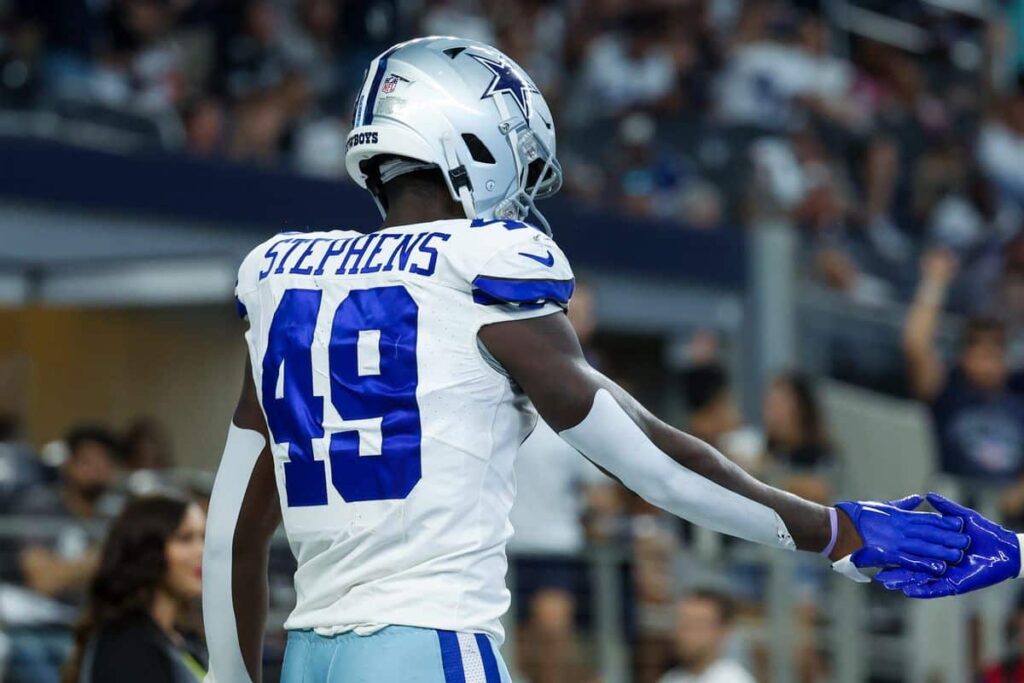 Football player #49, John Stephens Jr., wearing a Dallas Cowboys uniform, seen from the back, extending his hand for a handshake.