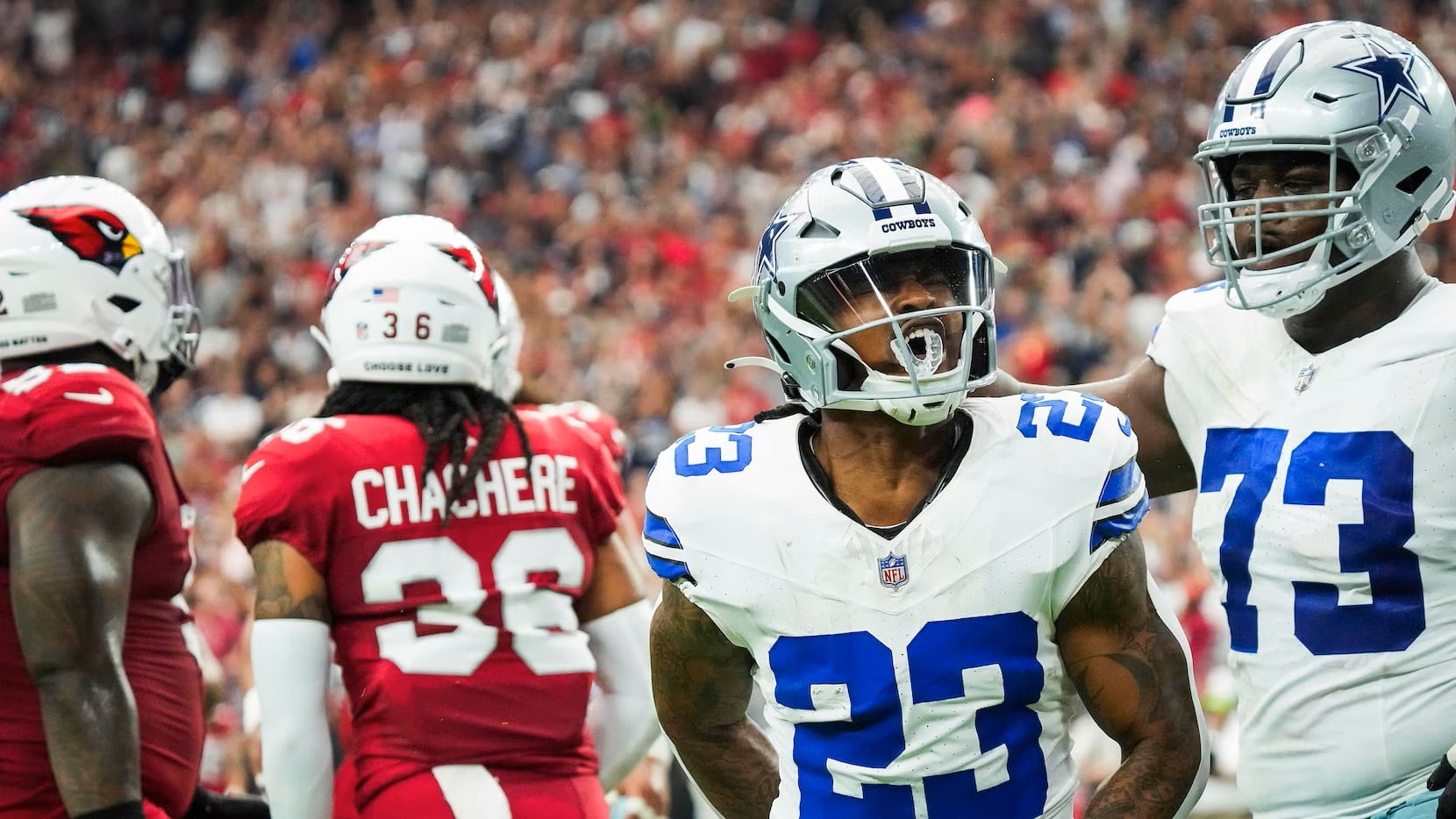 Football players from opposing teams on the field during a game, including Rico Dowdle in a Dallas Cowboys uniform.