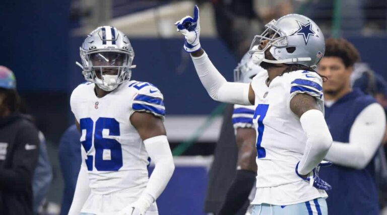 Two football players in Dallas Cowboys uniforms, including cornerback DaRon Bland, with one pointing upwards during a game.