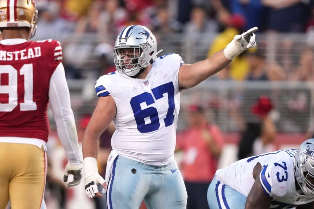 Dallas Cowboys player in a white uniform points during a game against the San Francisco 49ers, signaling to teammate Brock Hoffman.