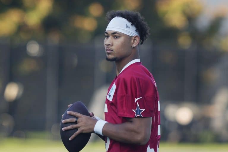 A football player in a red jersey holds a football, standing outdoors with a focused expression.