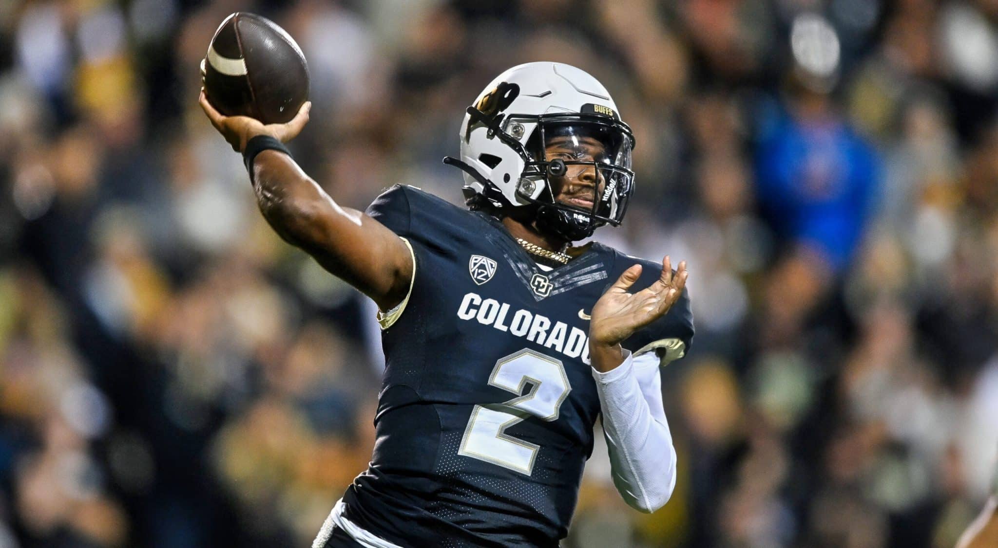 Football player in a black "Colorado" uniform and helmet throwing a pass during a game.