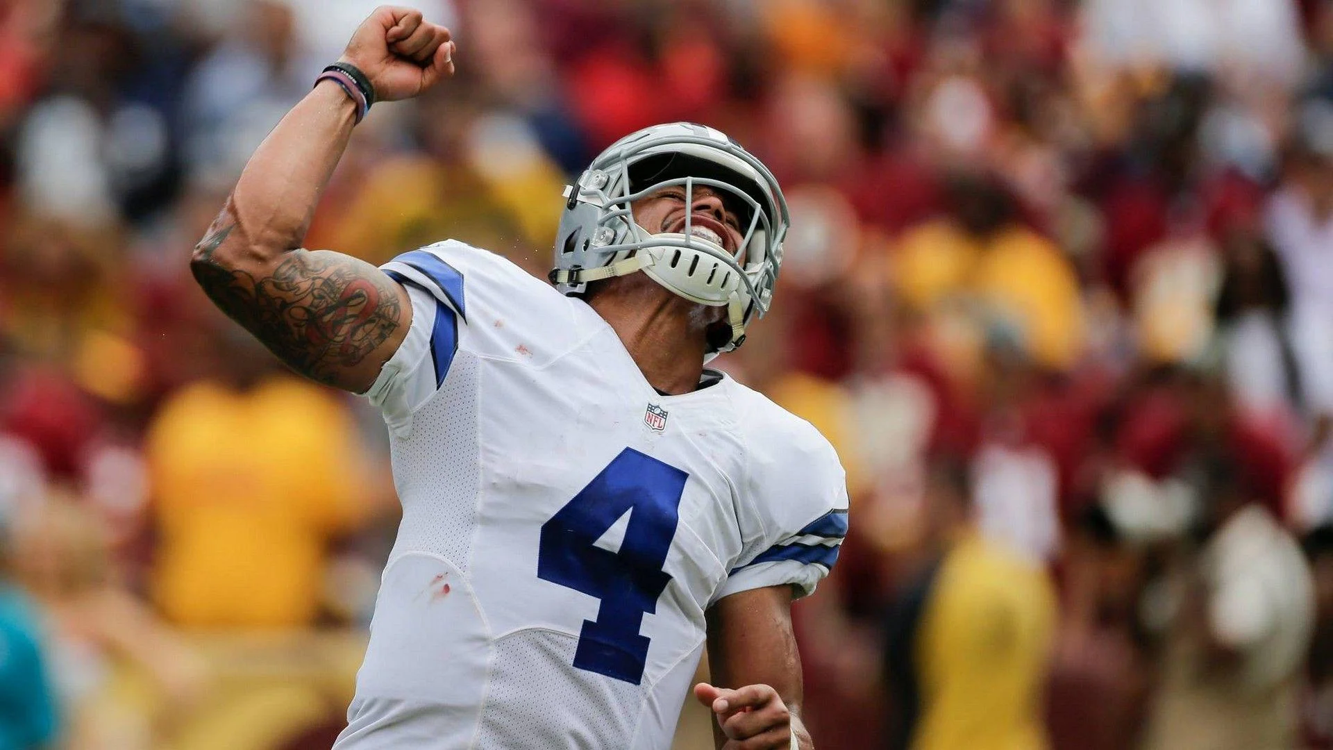 Football player in white Dallas Cowboys jersey number 4 with his arm raised, celebrating during a game.