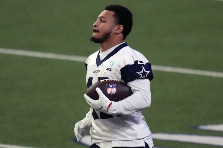 A football player in a white jersey holding a football on a field during a practice session.