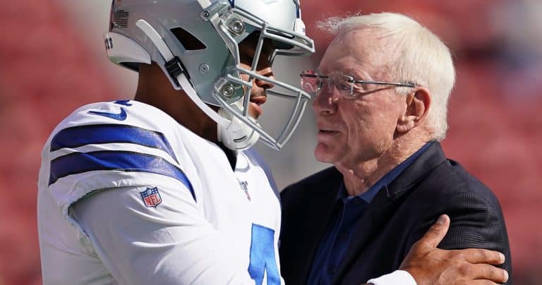 A football player in uniform and a man in a suit embrace on the field.