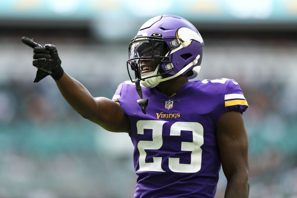 Football player Andrew Booth in a purple Vikings uniform and helmet points with his right hand during a game.