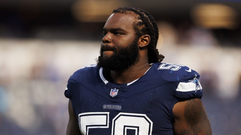 A football player in a Dallas Cowboys jersey stands on the field with a focused expression.