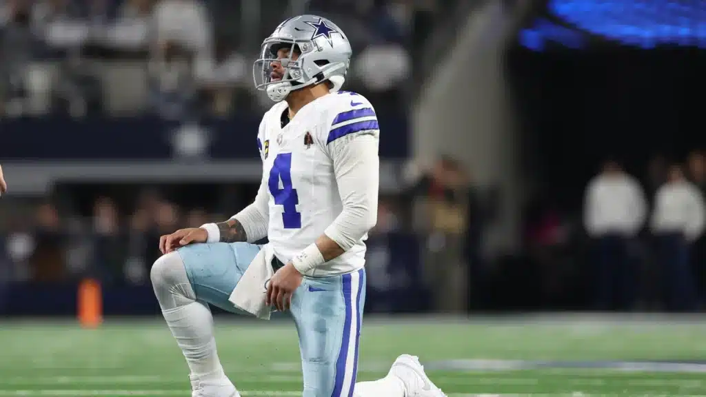 Football player in Dallas Cowboys uniform kneels on the field during a game.