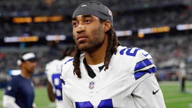 A football player in a white uniform with the number 21 stands on the field, looking ahead.