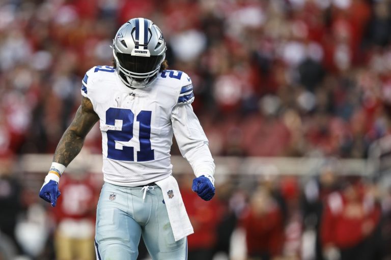 Football player in a blue and white uniform, wearing number 21, walking on a field with a crowd in the background.