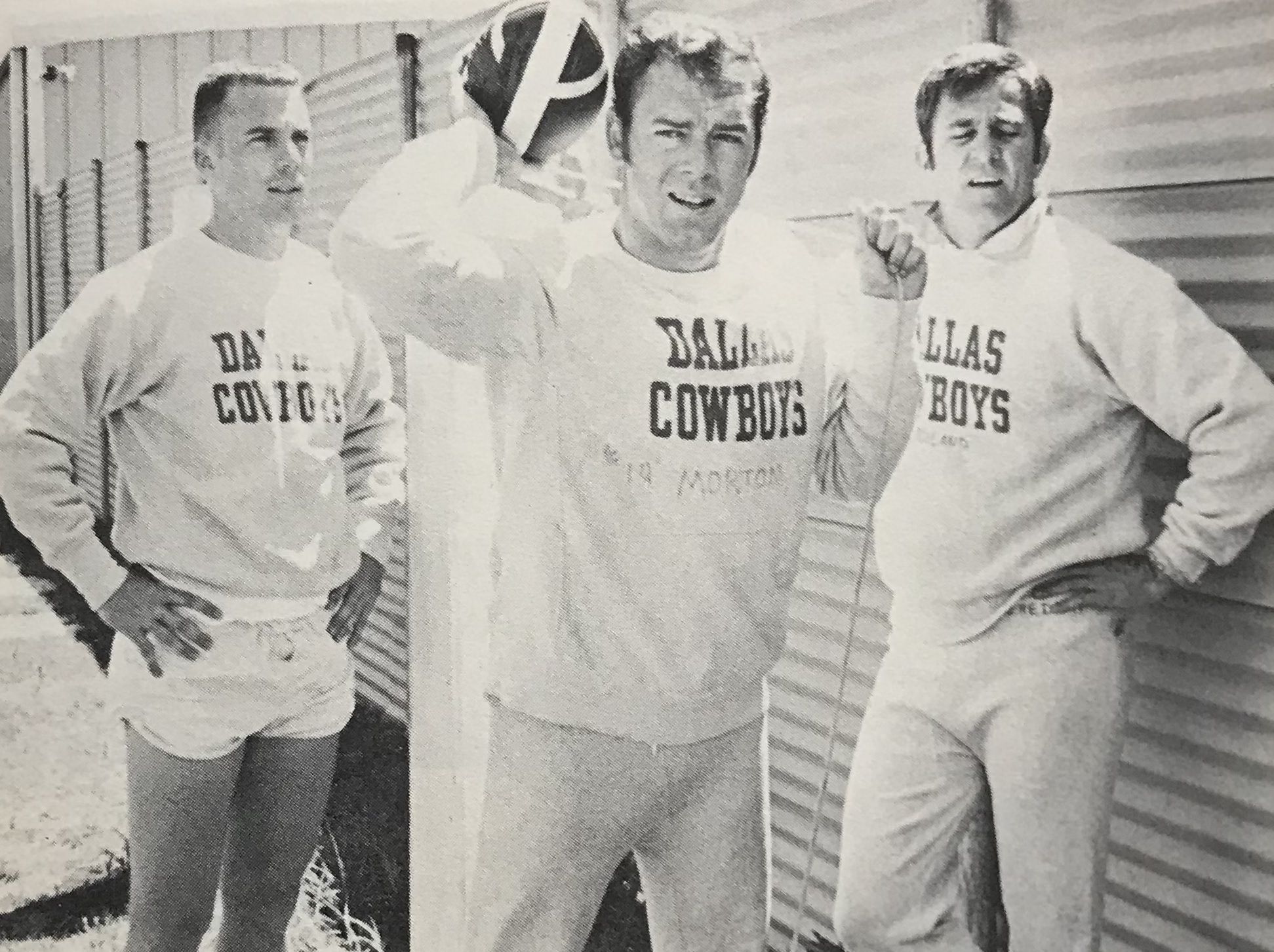 Three men wearing Dallas Cowboys sweatshirts pose outdoors, one holding a football near his shoulder.