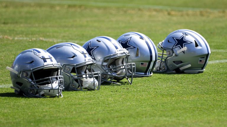 Four Dallas Cowboys football helmets lined up on a grassy field.