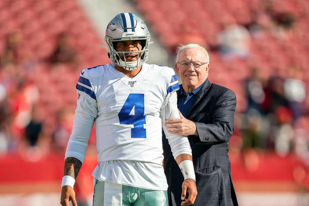 A man wearing a Dallas Cowboys football uniform stands next to an older man in a suit on a football field.